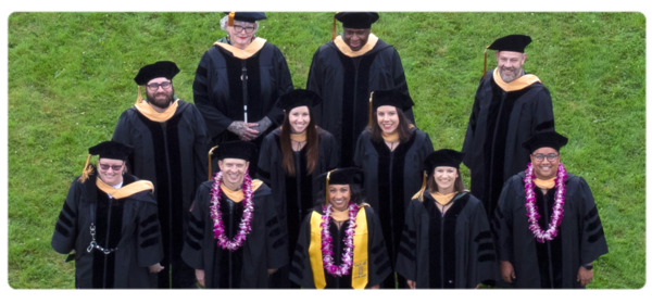 The first graduating DSW cohort in caps and gowns and hoods smiles up at the camera